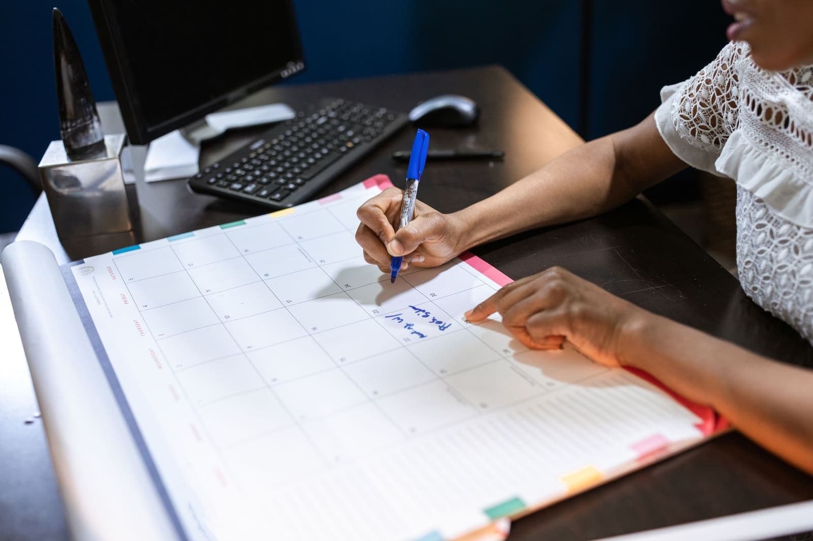 A woman writing an appointment into a desk calendar beside a keyboard
