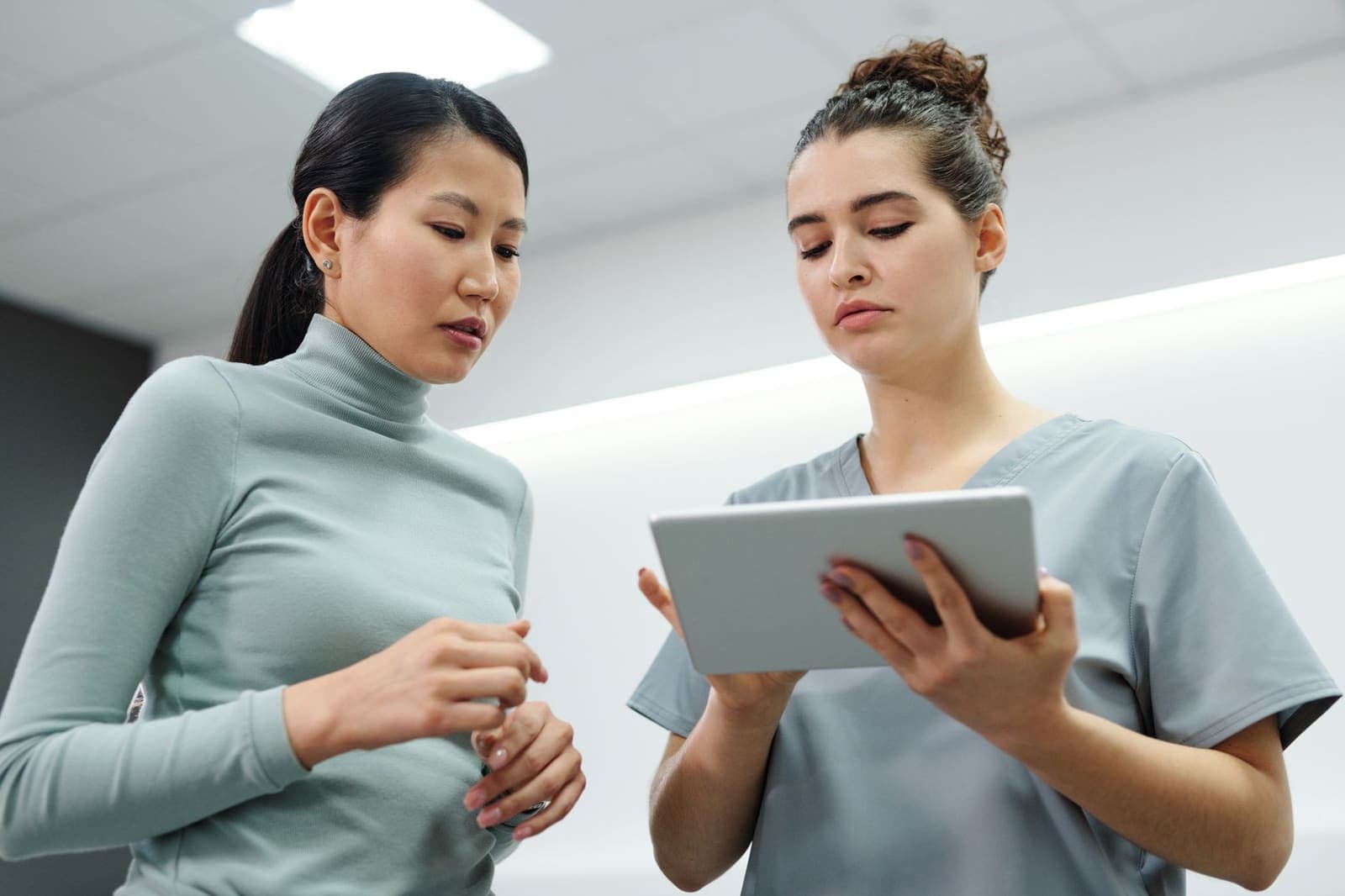 A clinic staff member in scrubs showing a tablet to a woman in a clinic corridor