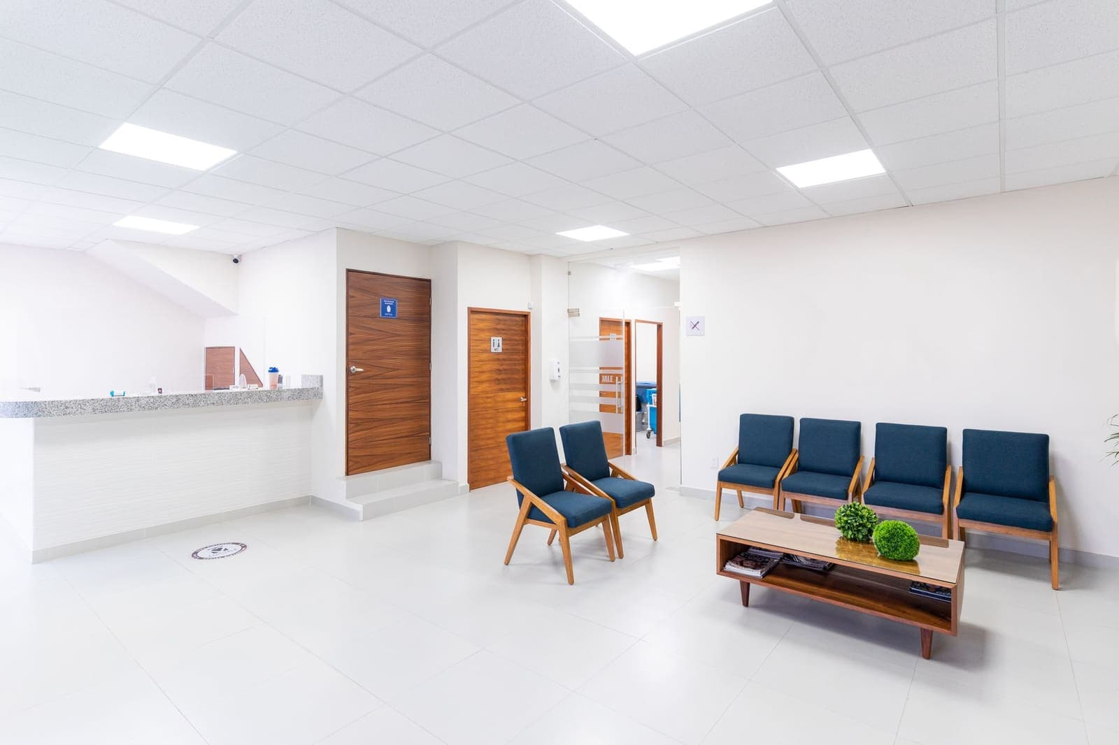 An empty, bright clinic waiting room with blue chairs and wooden doors