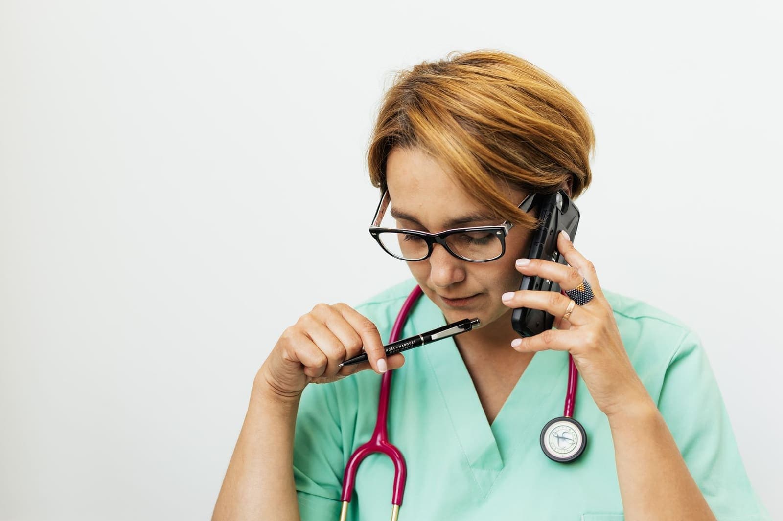A nurse in scrubs on a phone call, pen in hand