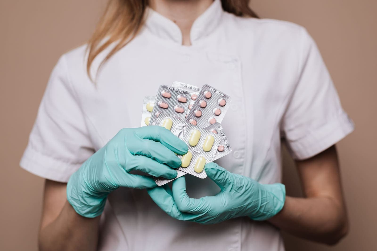 Gloved hands holding several blister packs of tablets against a white uniform