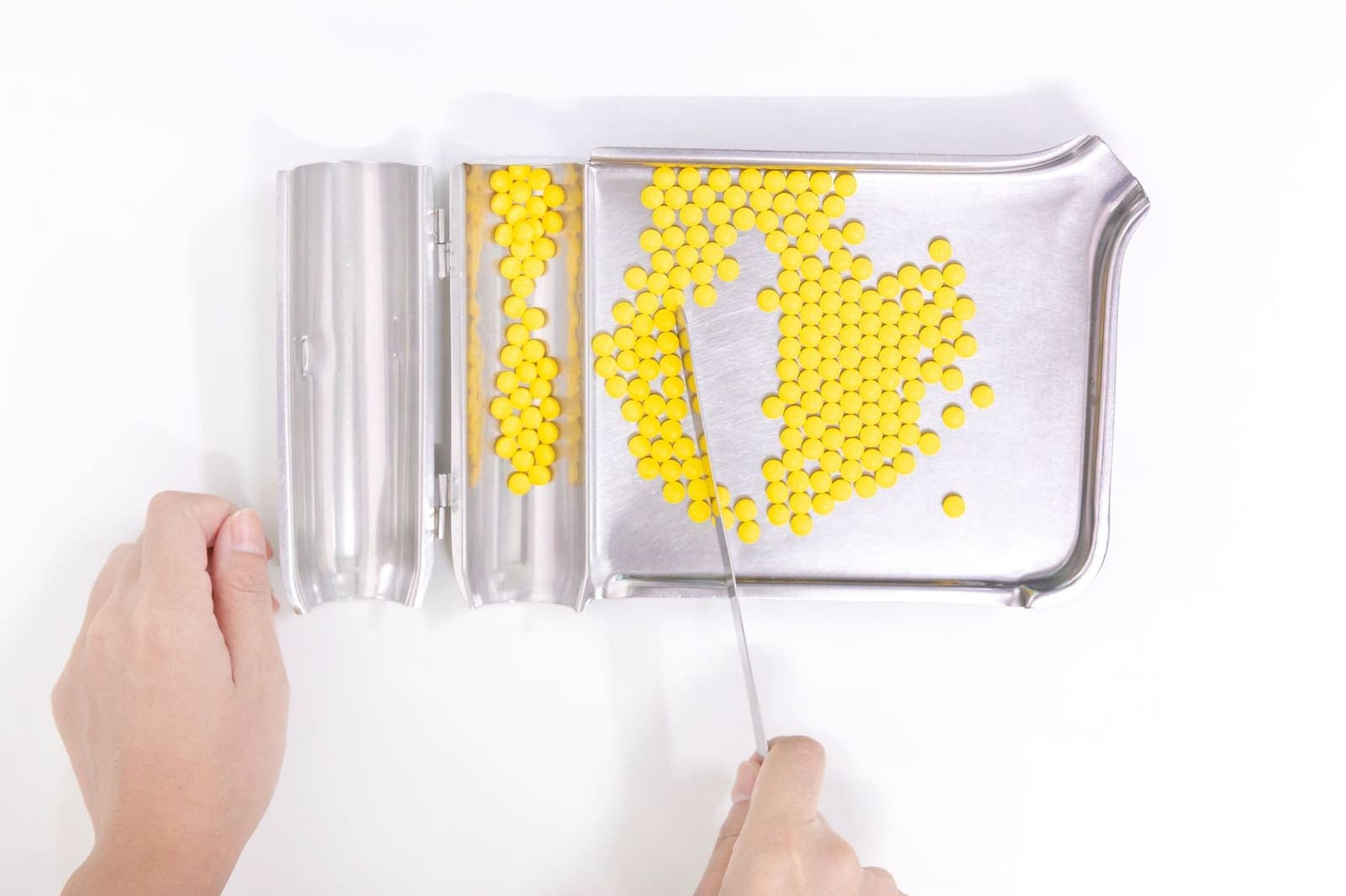 Hands counting yellow tablets on a stainless steel pill counting tray with a spatula