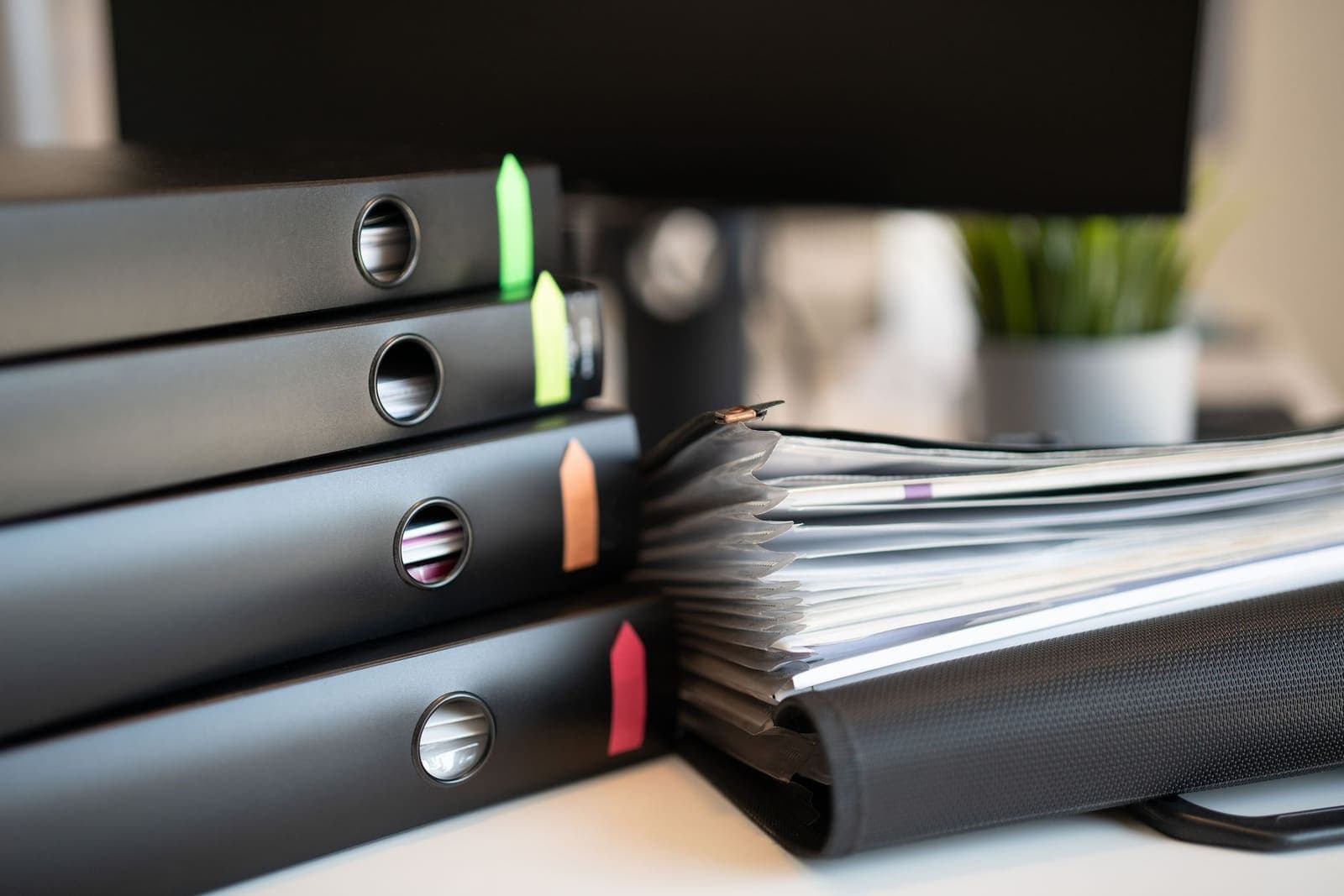 A stack of black ring binders with coloured tabs beside an expanding file on a desk