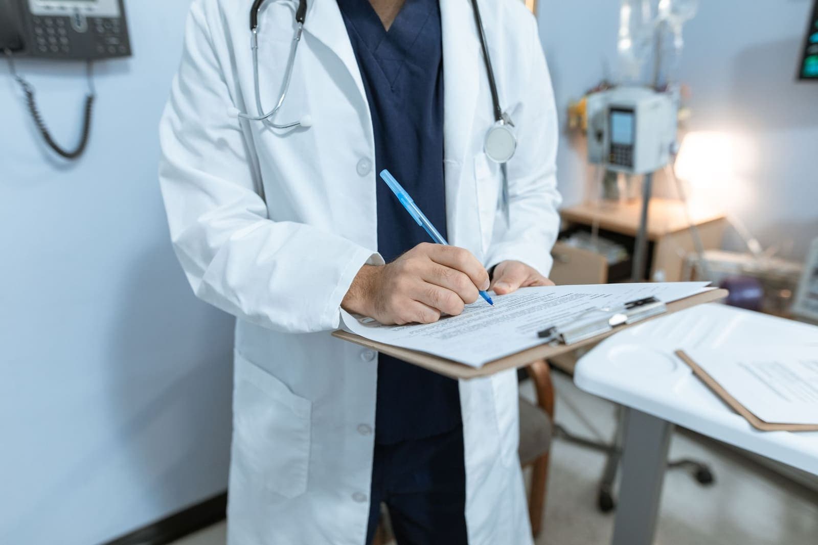 A doctor in a white coat writing on a clipboard in an exam room