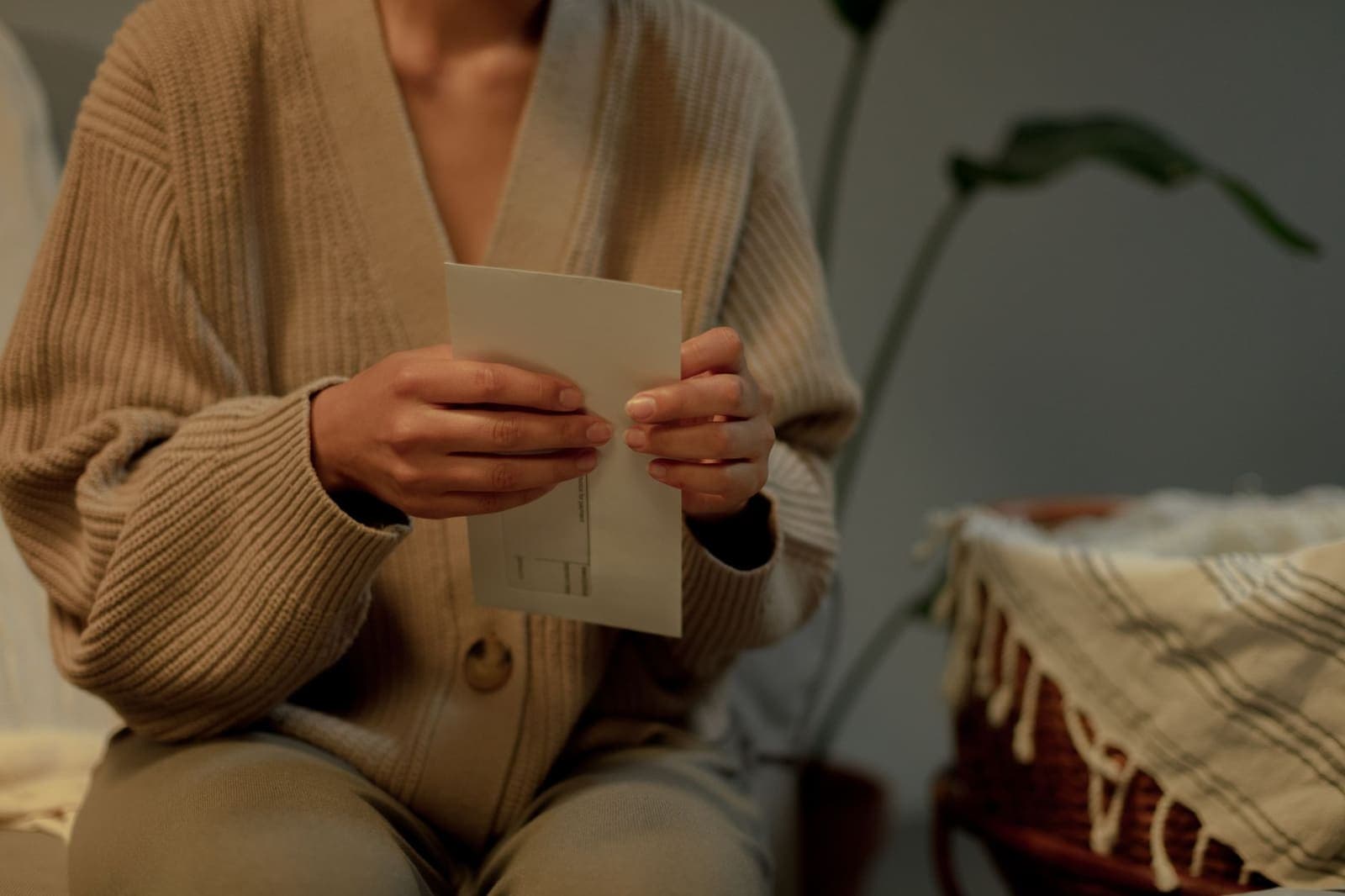 A person in a beige cardigan sitting at home holding an opened letter in both hands
