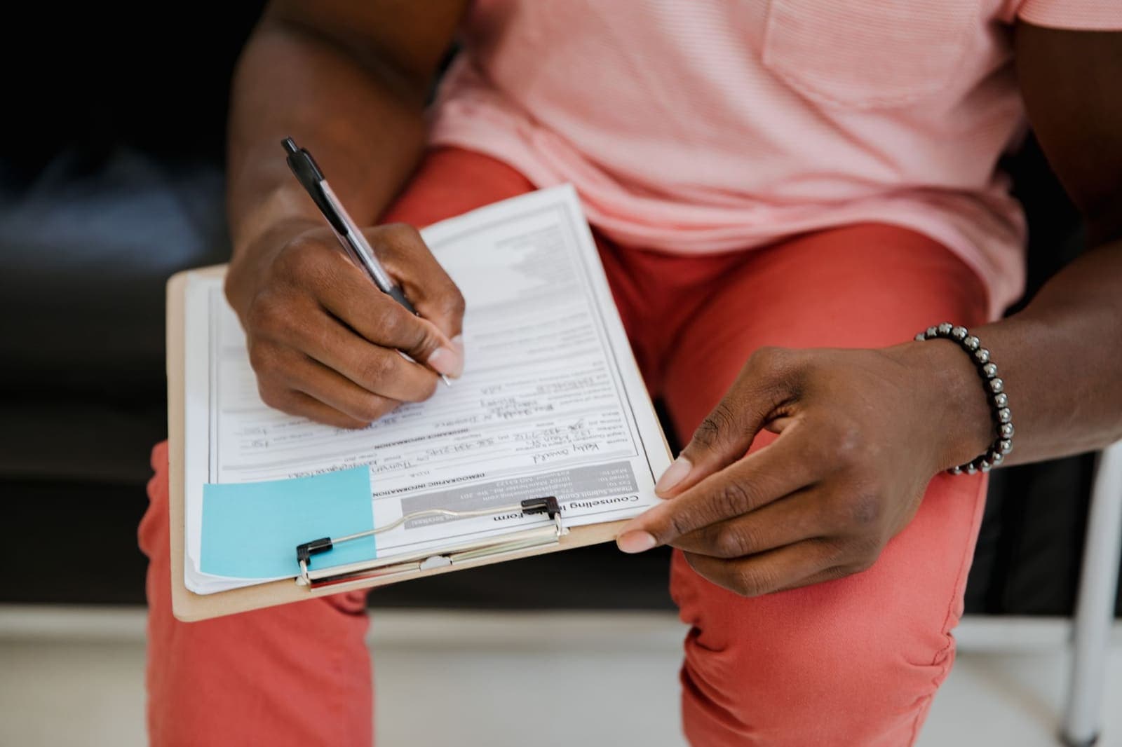 A seated patient fills in an intake form on a clipboard