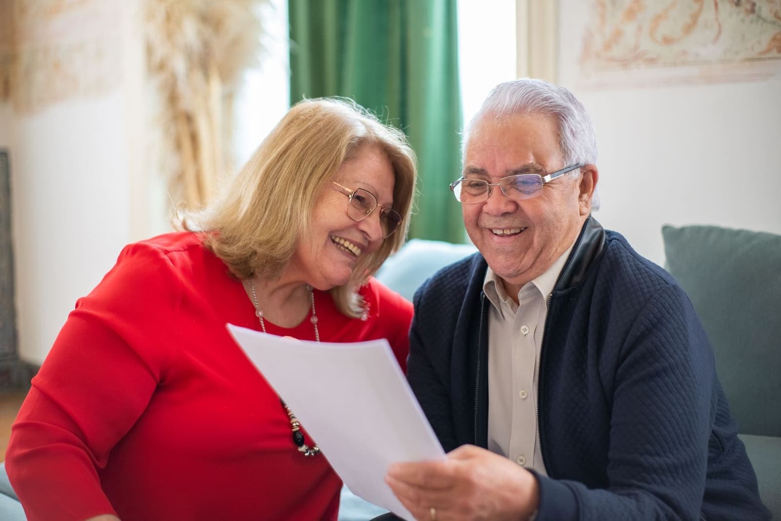 An older couple smiling as they read a printed letter together at home
