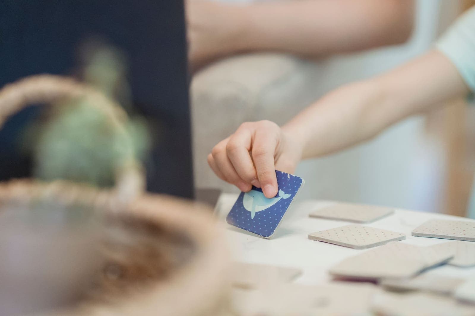 A child's hand turning over a picture card showing a whale in a memory matching game on a white table