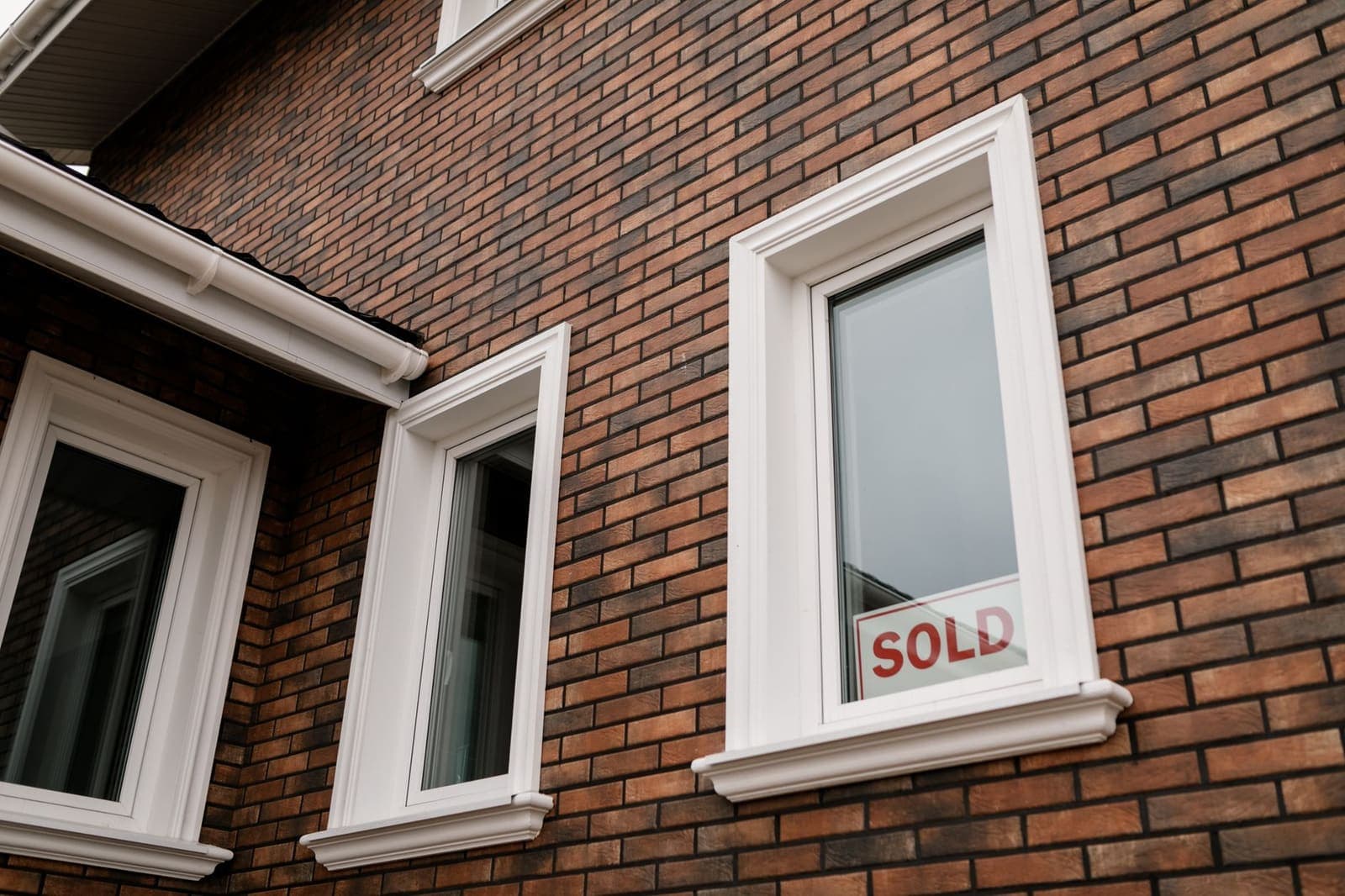 A Sold sign in the window of a red brick house with white window frames