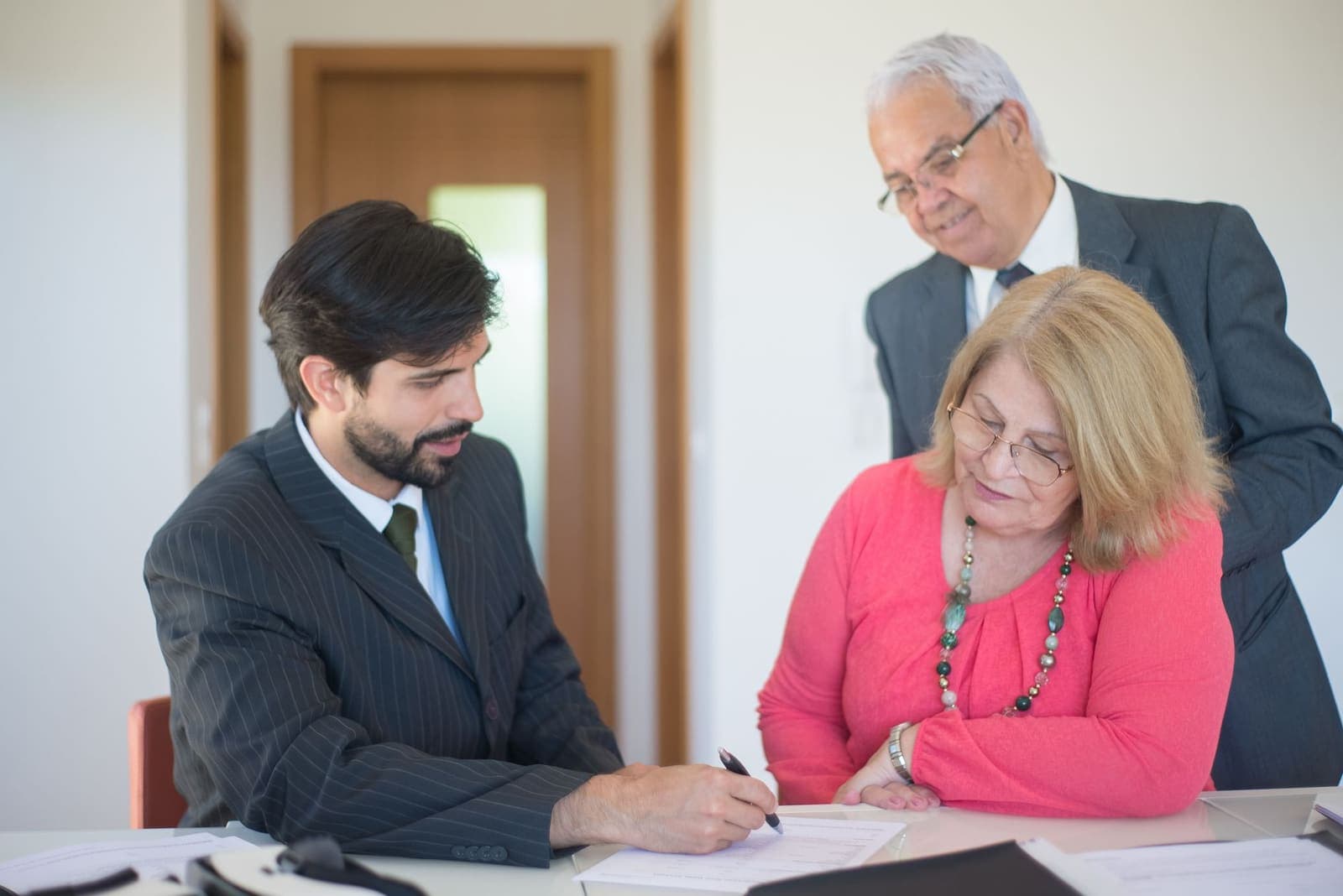 An agent and two clients reviewing and signing property documents at a table