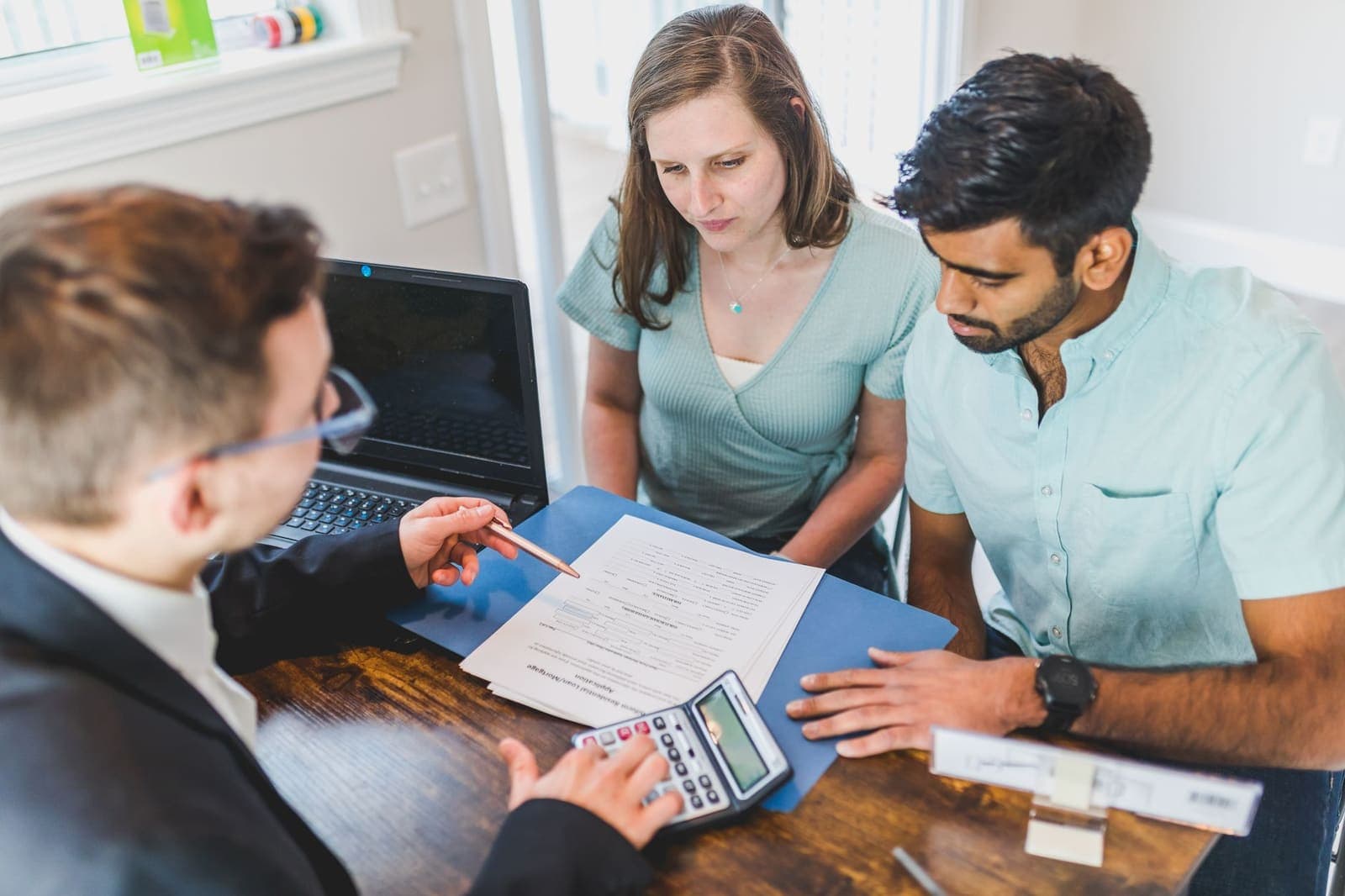 A loan officer walks a couple through a mortgage application at a desk with a calculator and laptop