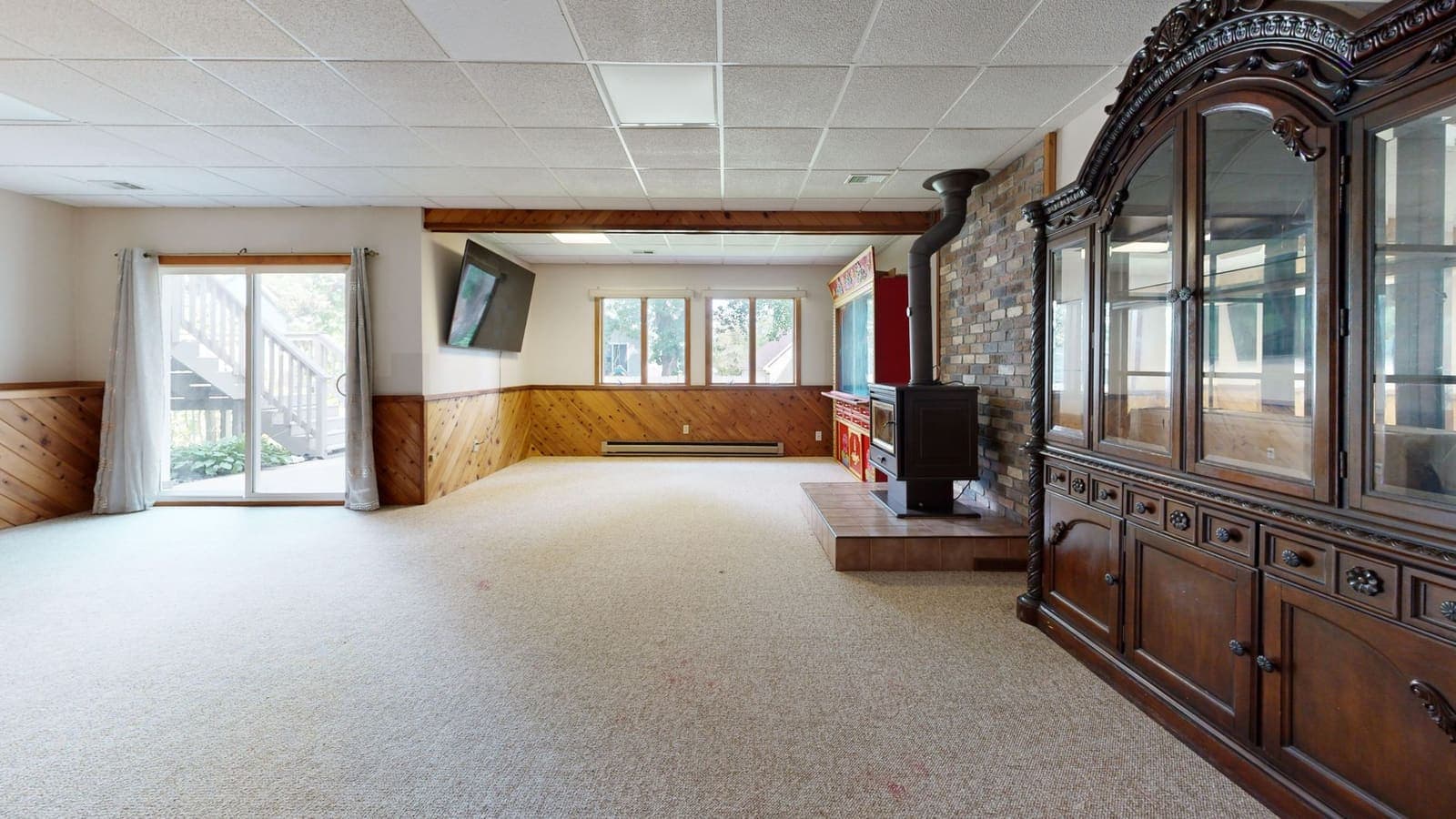 A carpeted lower-level family room with wood paneling, a wood stove on a brick hearth and a sliding door to a walk-out patio