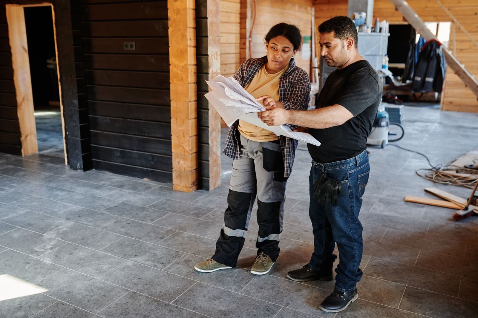 Two tradespeople on a renovation site reading through a stack of plans and paperwork together