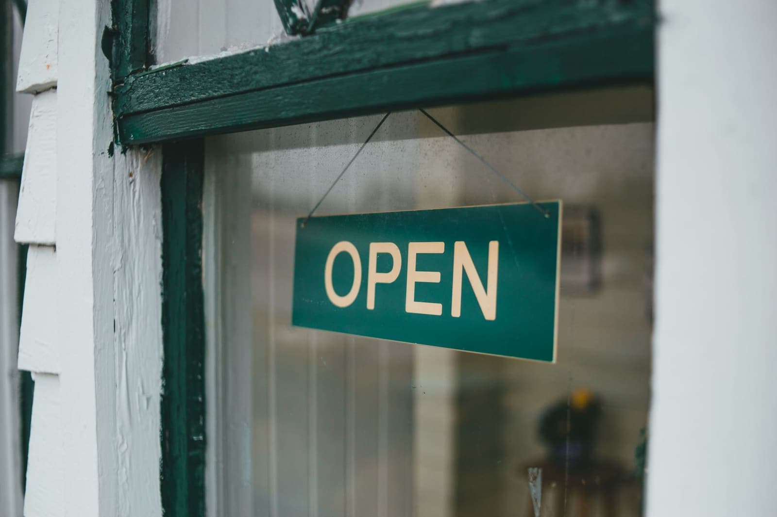 A green and cream OPEN sign hanging inside the glass of a painted wooden shop door