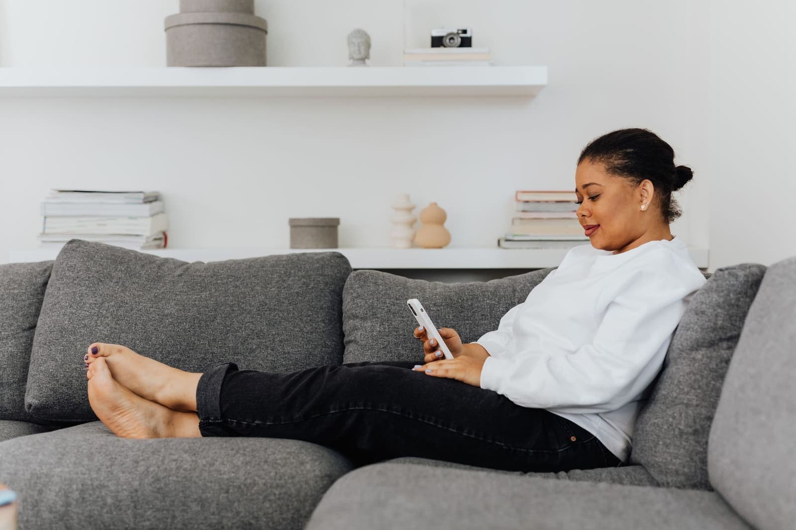 A woman sitting on a grey sofa with her feet up, reading something on her phone
