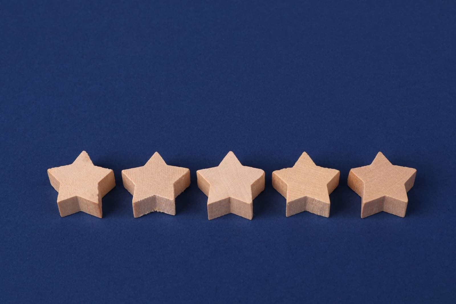 Five plain wooden star shapes in a row on a dark blue background