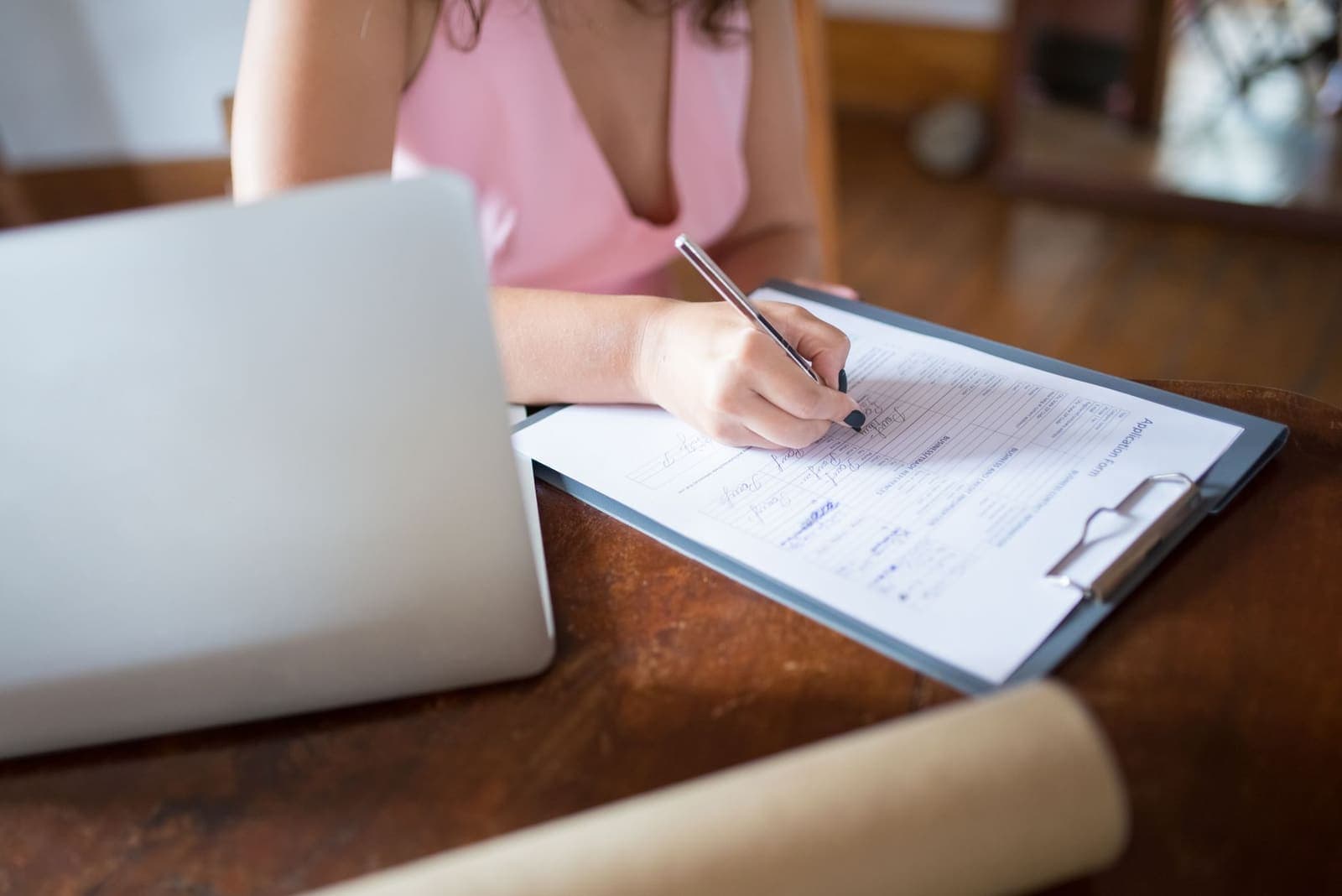 A person filling in a paper application form on a clipboard beside a laptop