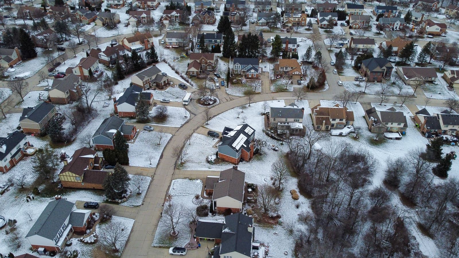 Aerial view of a snow-dusted subdivision in Novi, Michigan, with brick colonial houses along a curving street