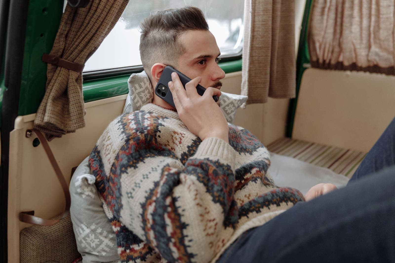 A man wrapped in a heavy patterned sweater talking on a mobile phone in a cold room