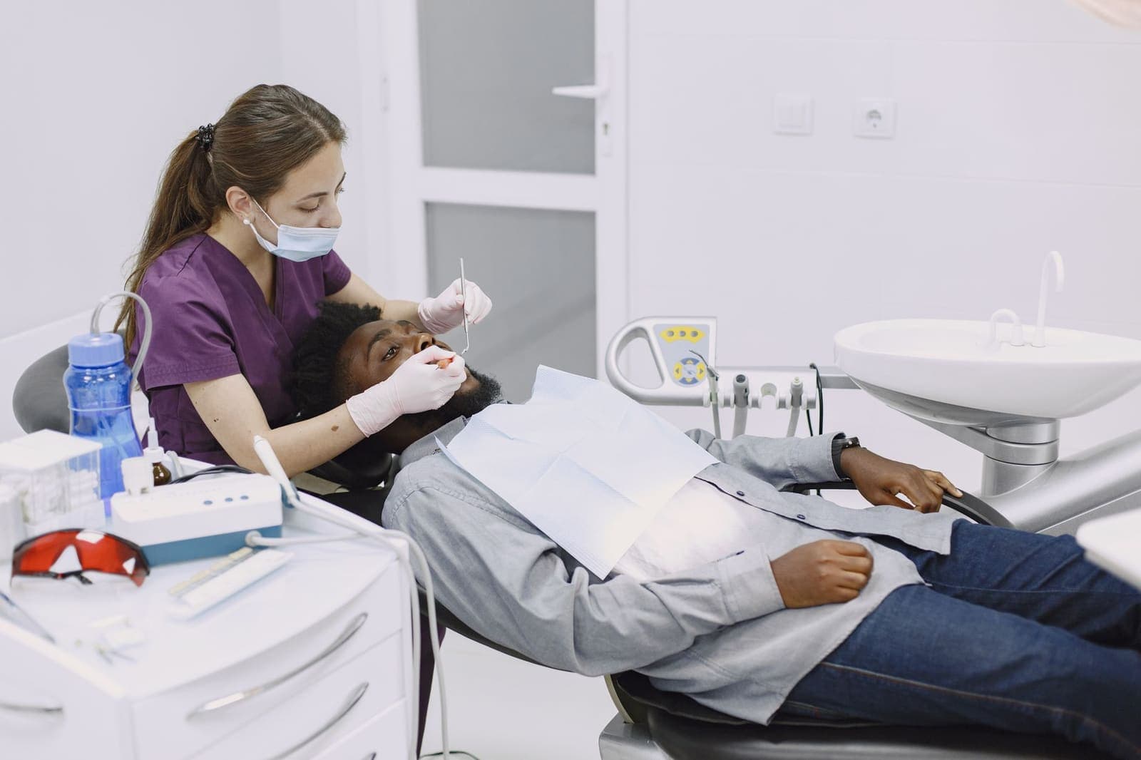 A dentist in a mask and gloves examining a patient reclined in the chair