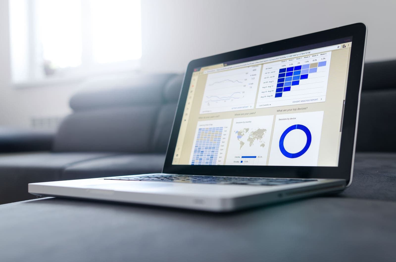 A laptop on a sofa showing an analytics dashboard with a line chart, a map and a donut chart