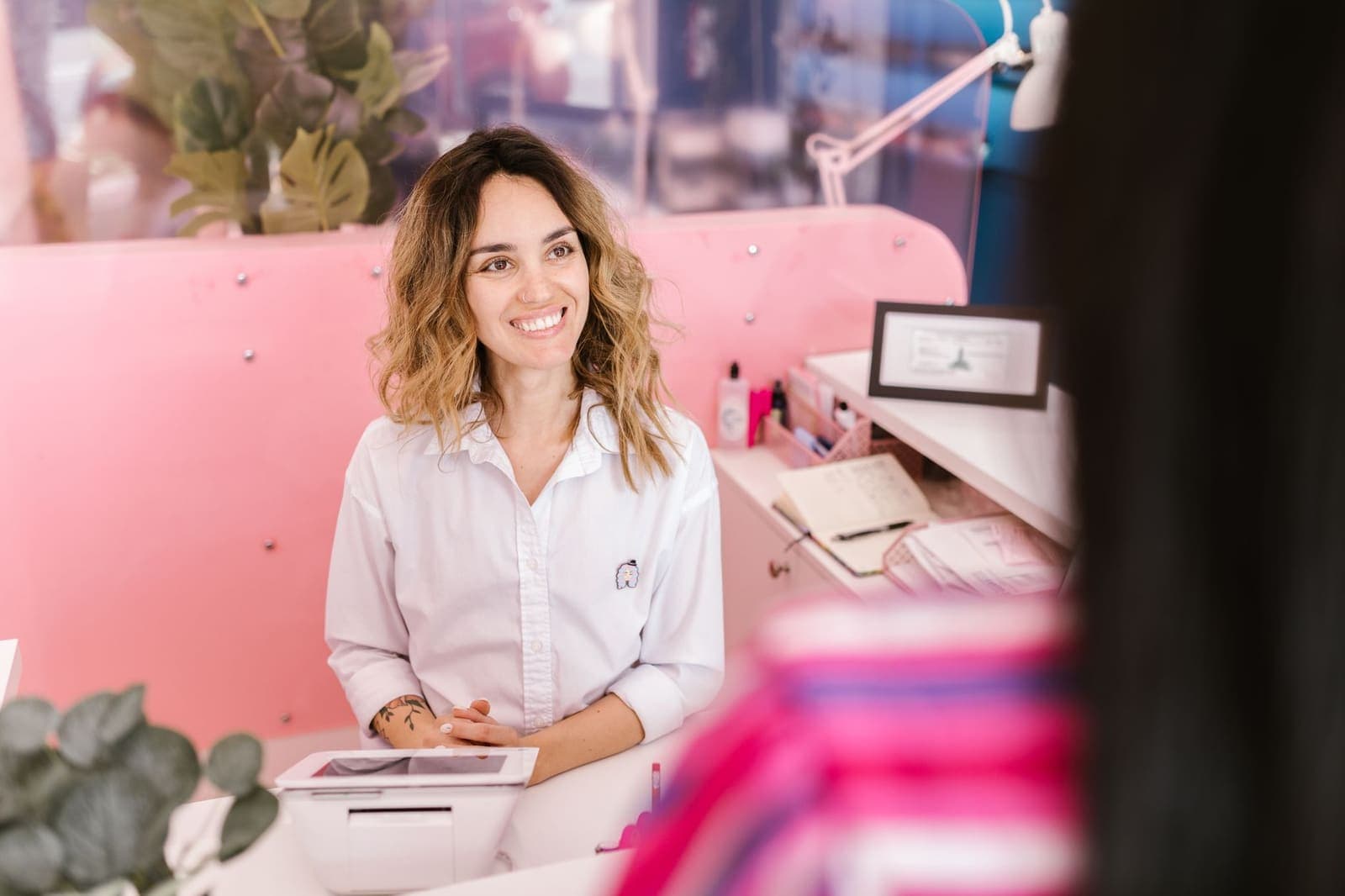A smiling receptionist behind the front desk of a salon, a tablet in front of her