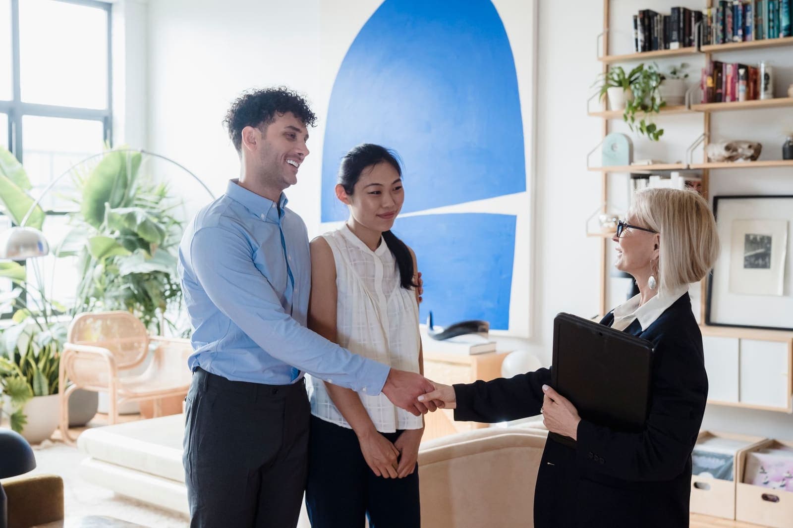 A couple shaking hands with an adviser in a bright living room