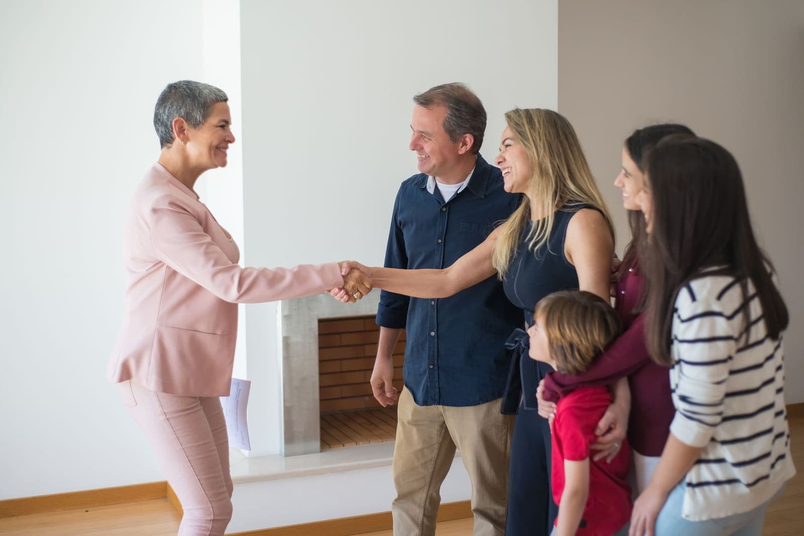 An agent shaking hands with a family in the empty living room of a new home