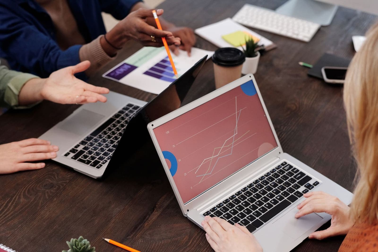 Hands pointing at a rising line chart on a laptop during a meeting