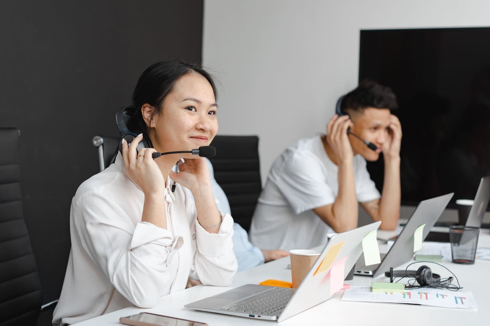 Two customer support agents at laptops with headsets in a small office