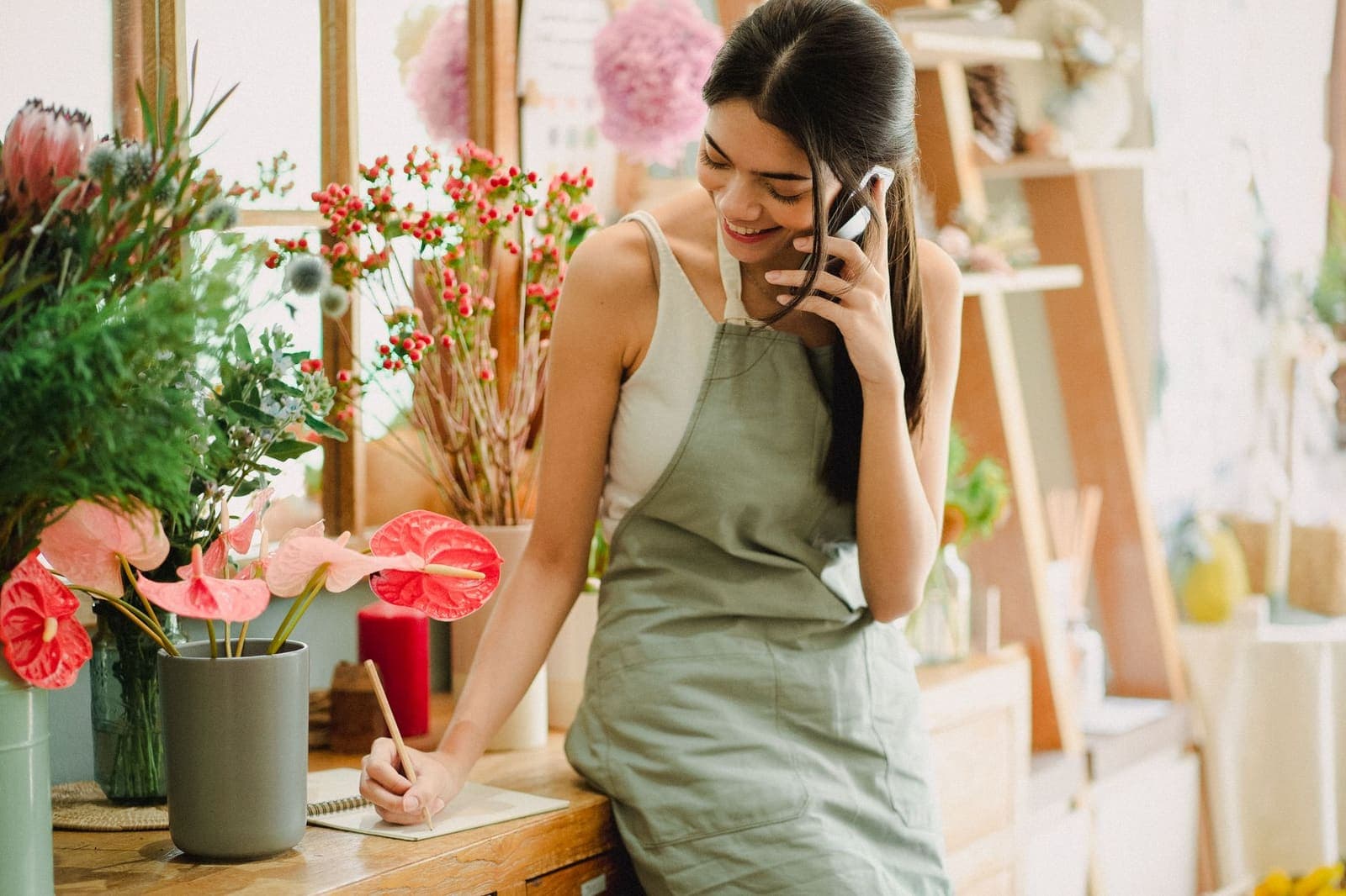 A florist in an apron taking a phone call at the counter of her shop