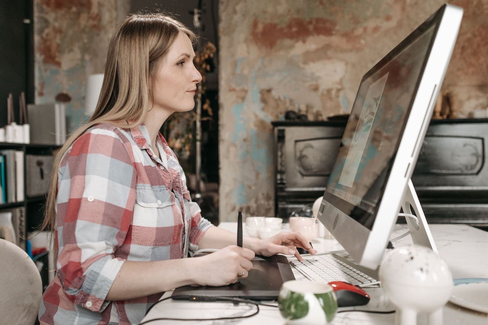 A designer in a plaid shirt working with a drawing tablet at a large monitor