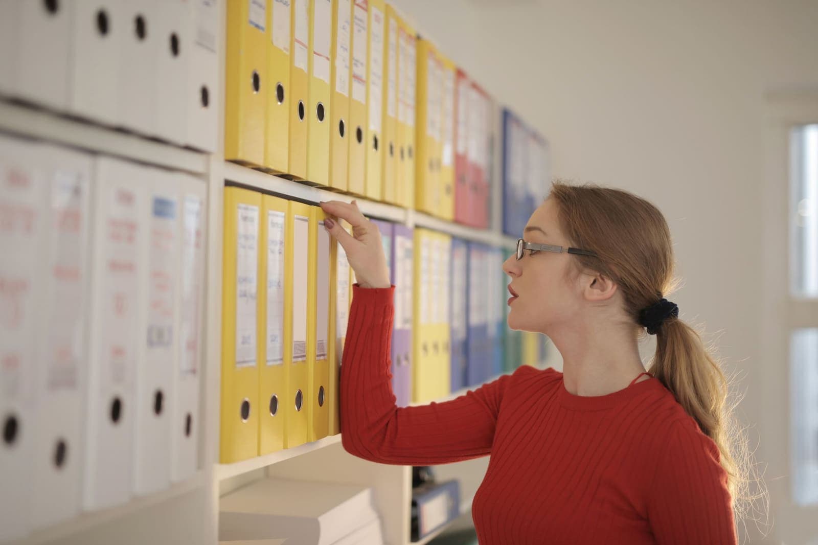 A woman searching through a wall of coloured binders in an office