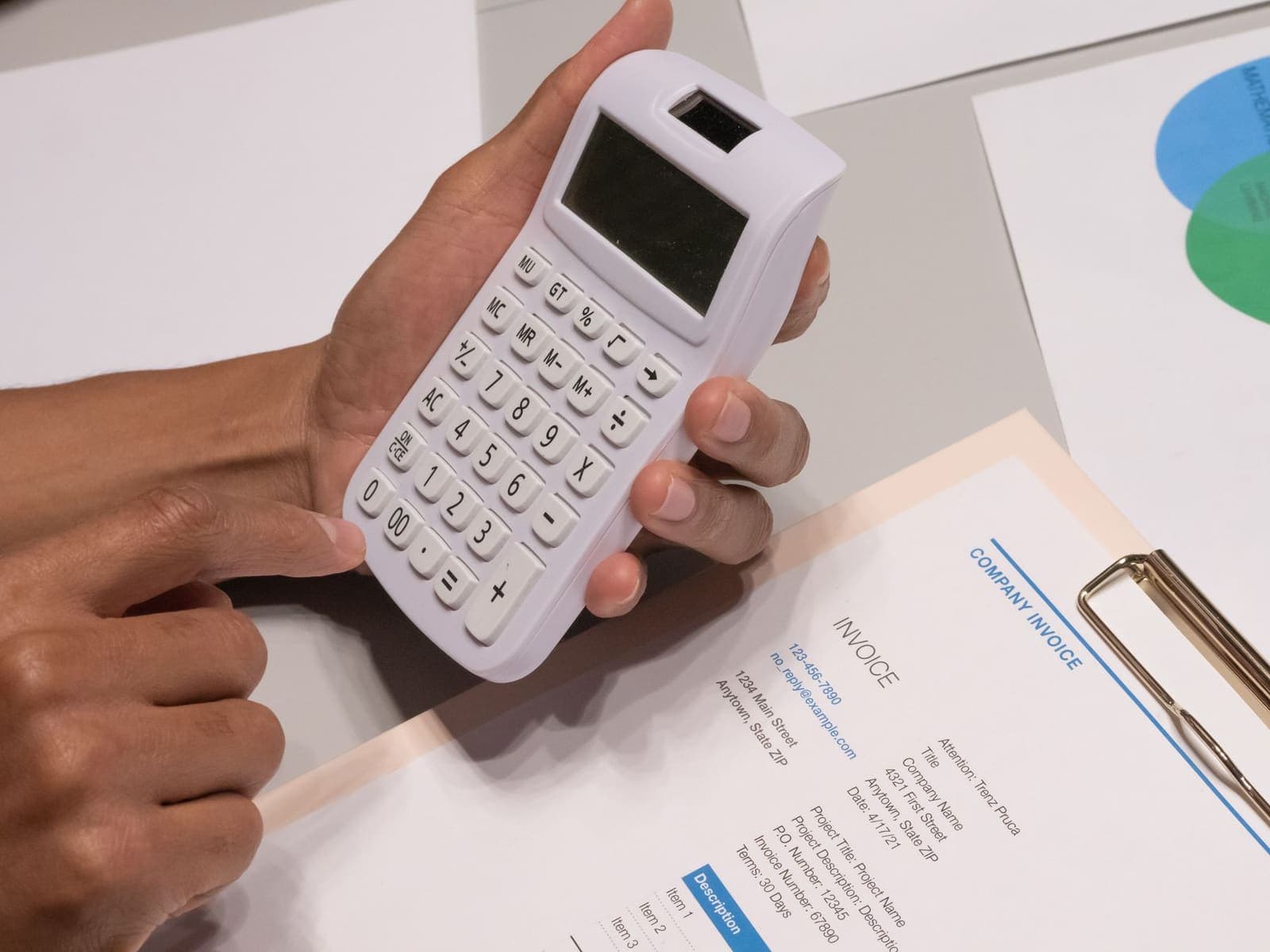 Hands using a calculator beside a printed invoice on a clipboard