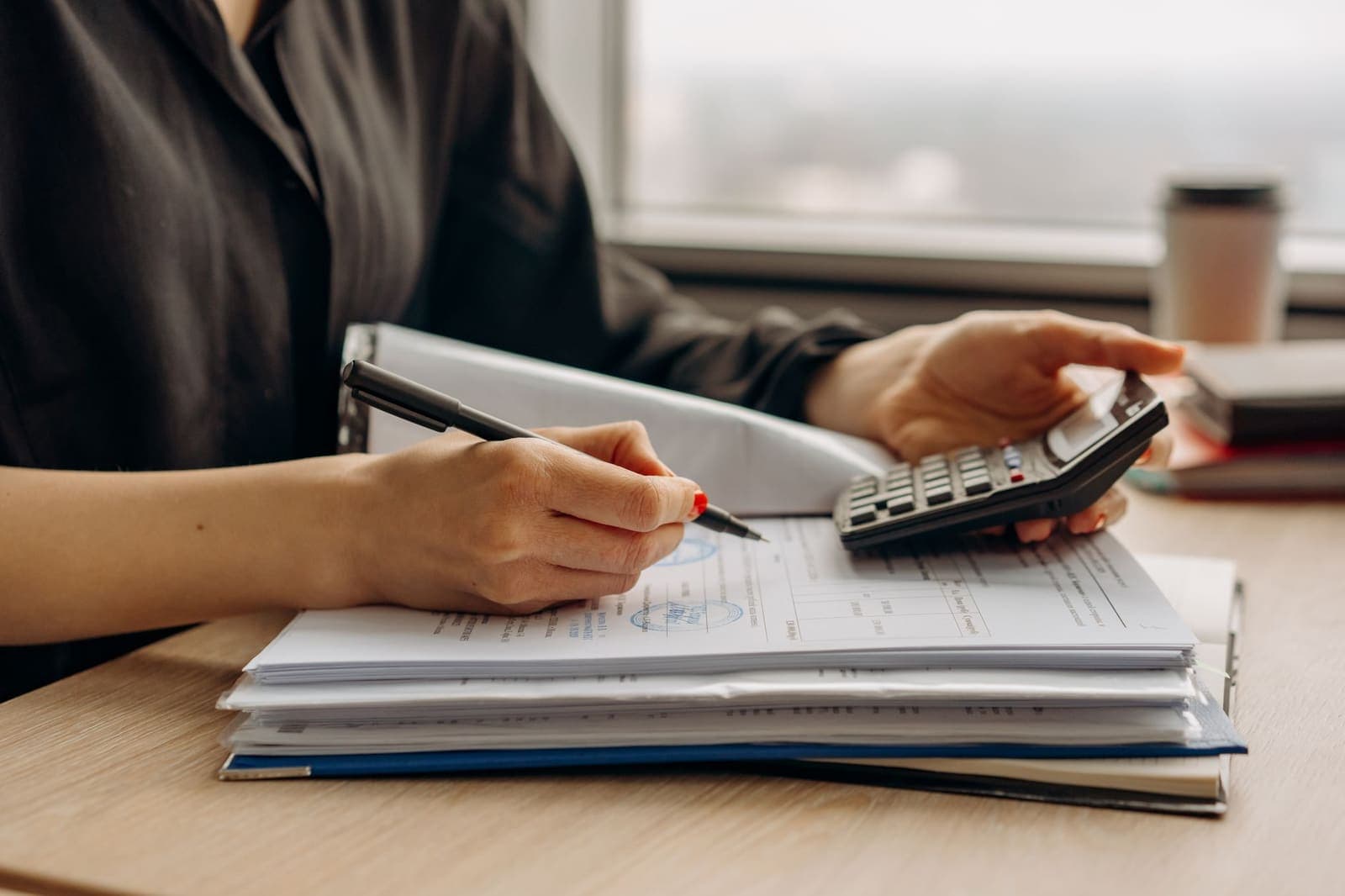 A person working through a binder of paperwork with a pen and a calculator