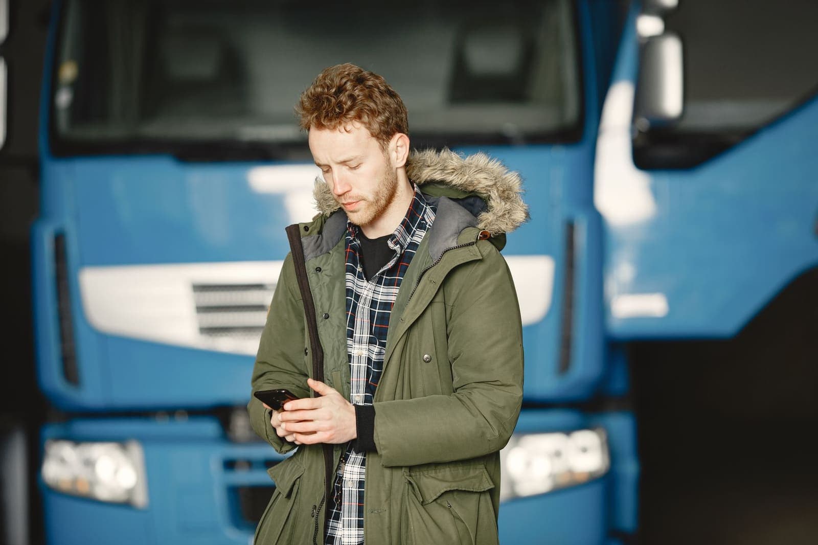 A man in a parka checking his phone beside a blue truck