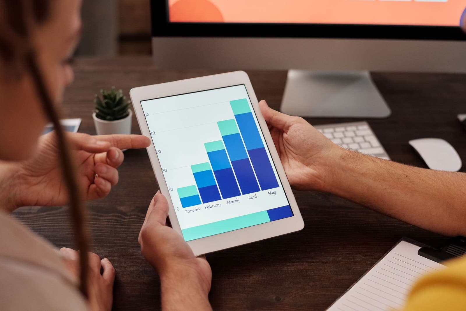 Two people looking at a rising bar chart on a tablet at a desk