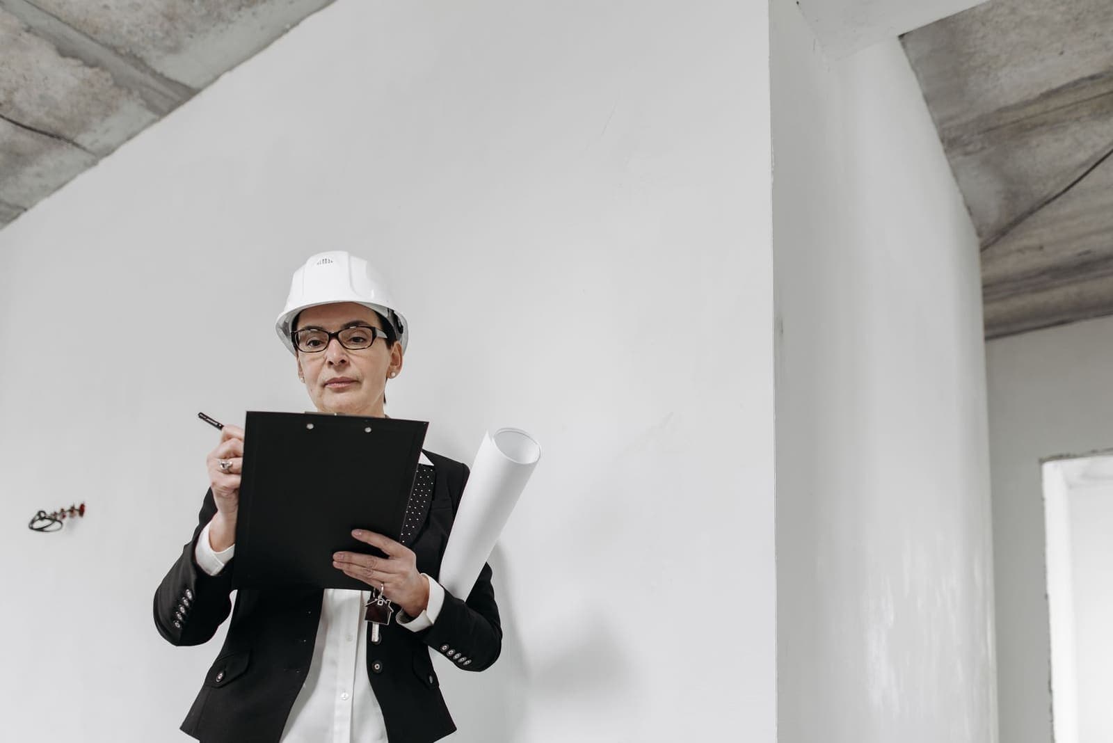 A construction engineer in a hard hat holding a clipboard and rolled plans on site