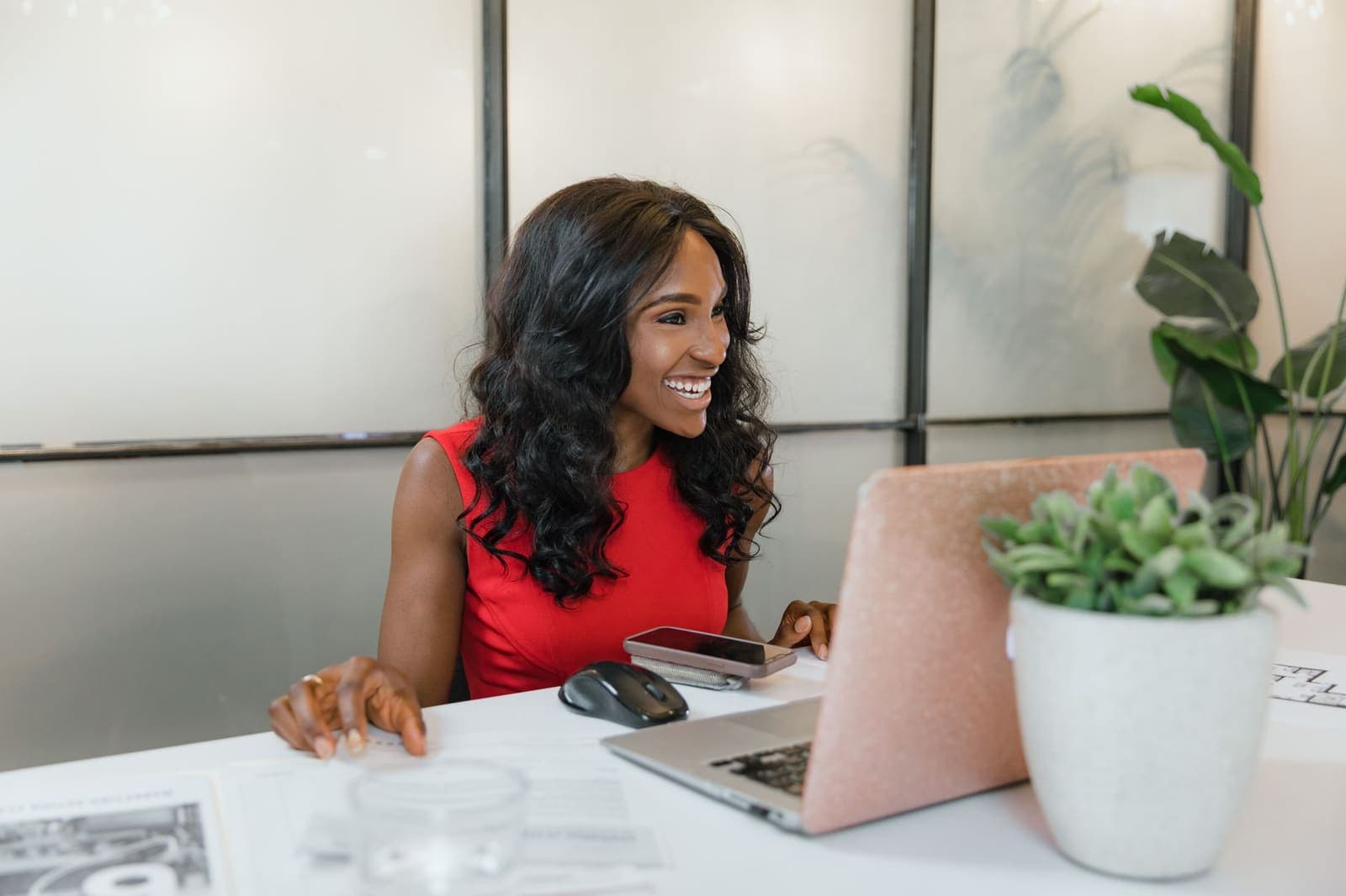 A woman at an office desk smiling at her laptop, phone beside her