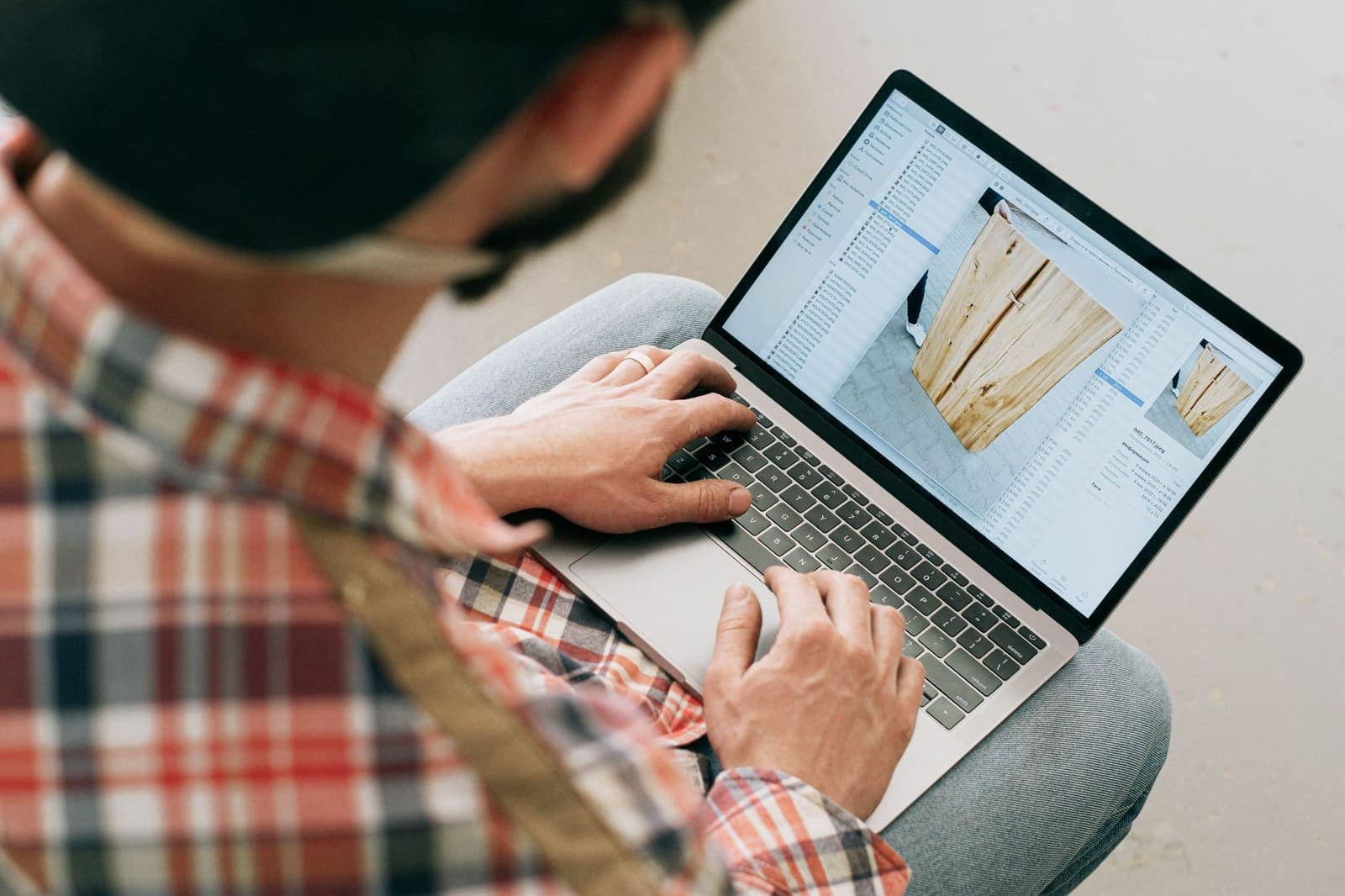 A craftsman in a plaid shirt working on a laptop in his workshop