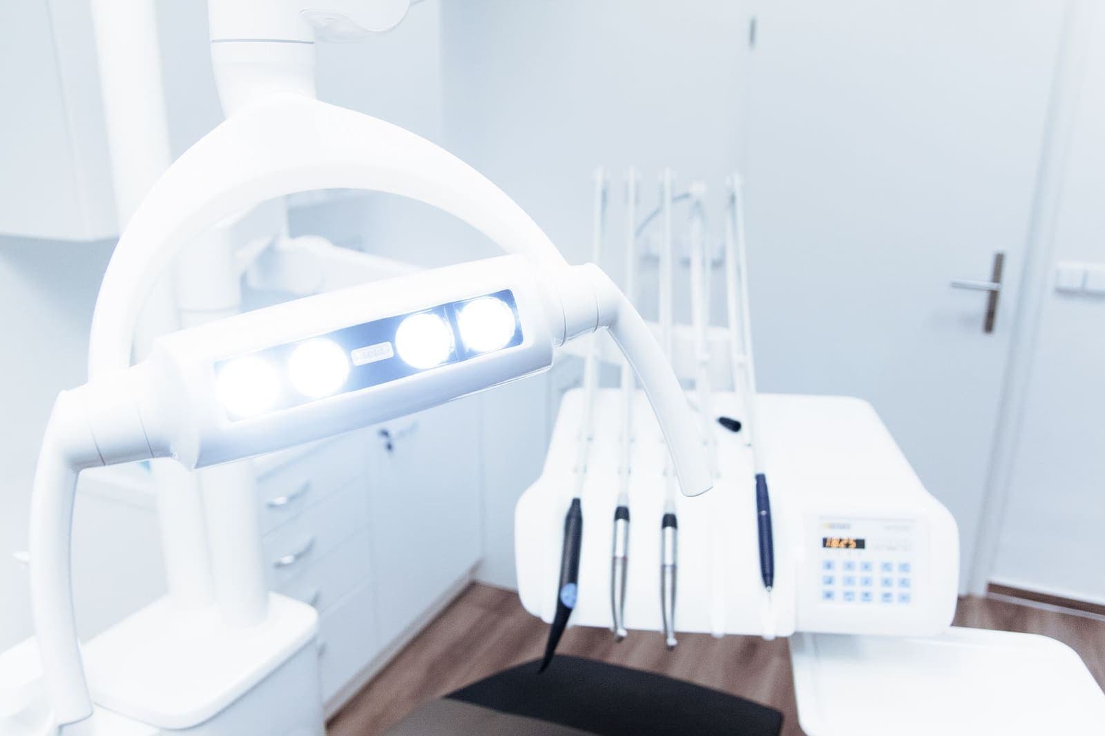 A bright dental operatory with the overhead light on, handpieces on the delivery unit and white cabinets