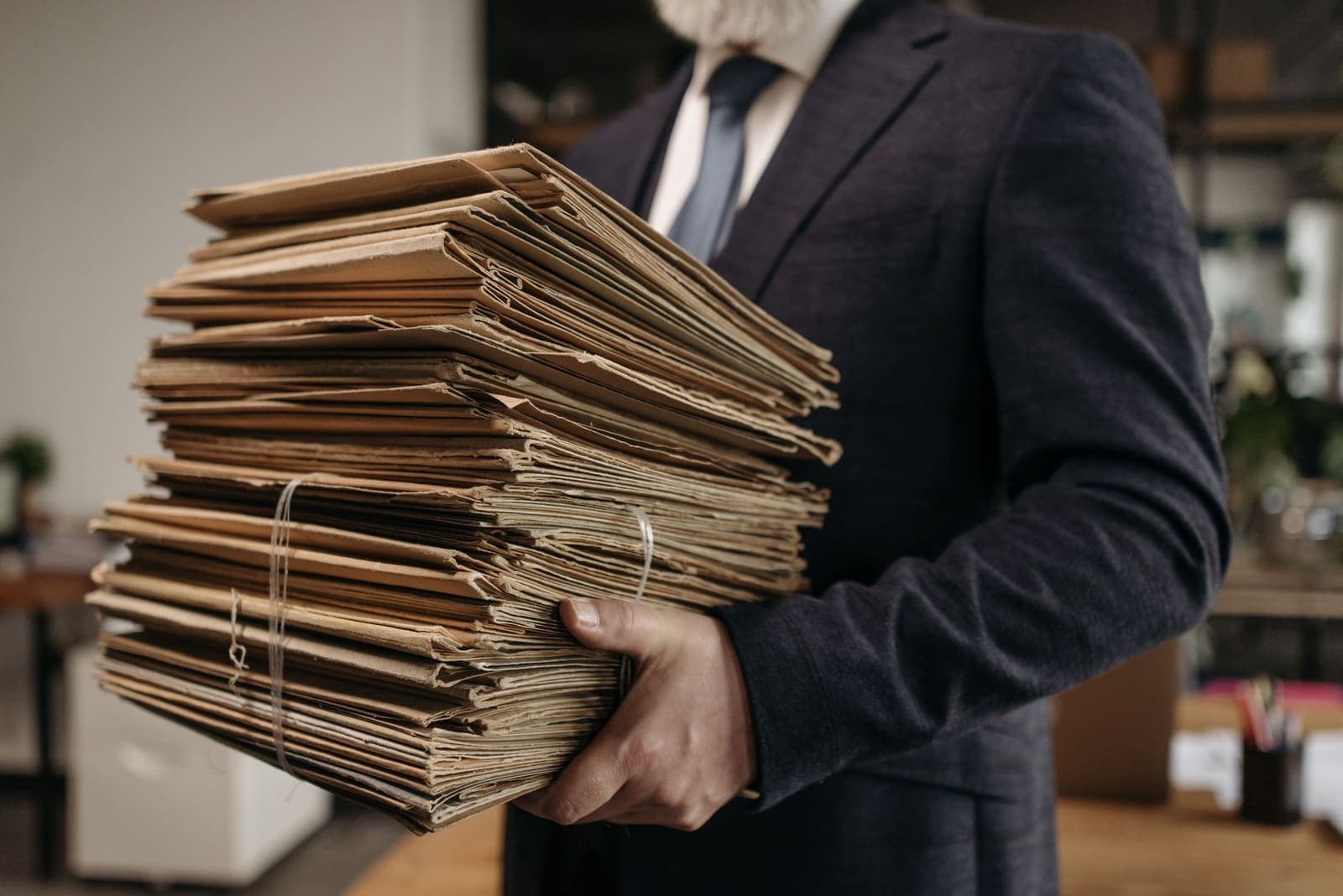A person in a suit carrying a tall stack of worn manila folders tied with string