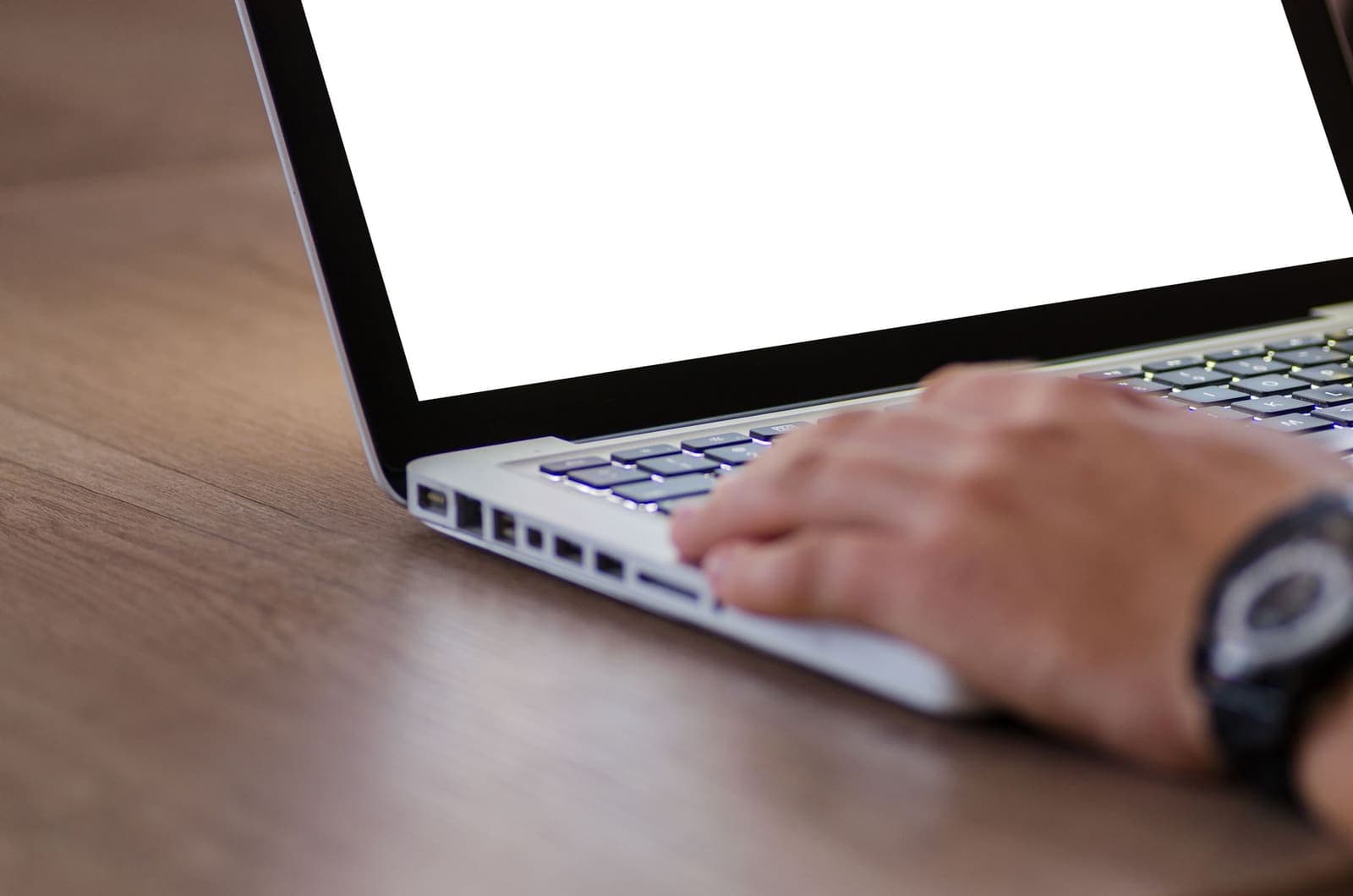 A hand resting on the keyboard of an open laptop on a wooden desk