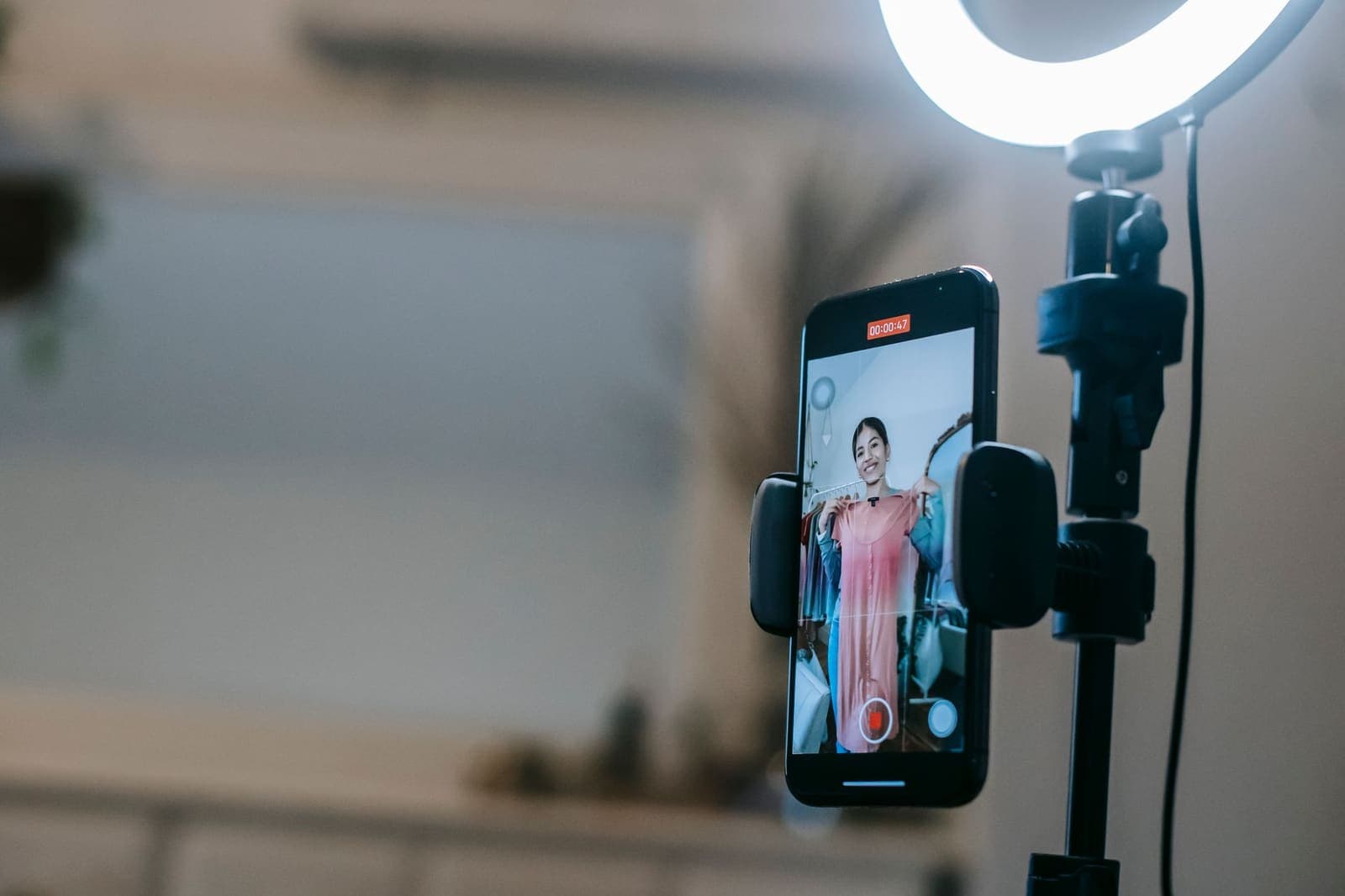 A phone on a ring light recording a shop owner holding up a dress