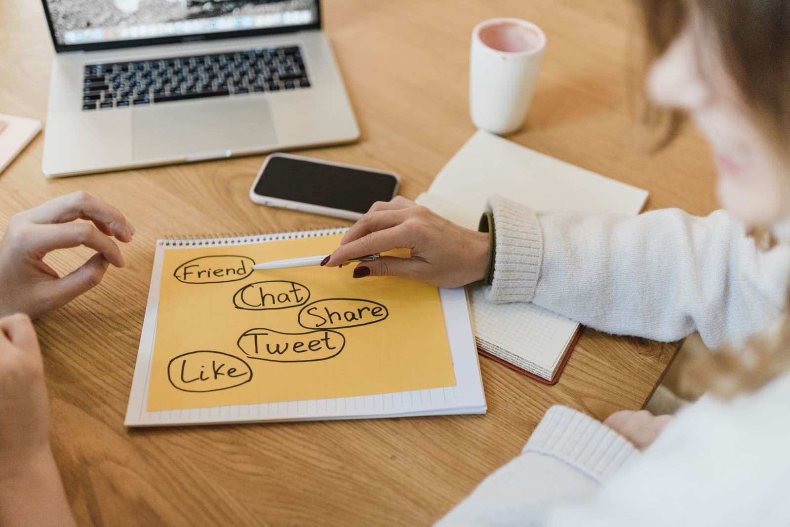 Two people planning social media content on a notepad beside a laptop and phone